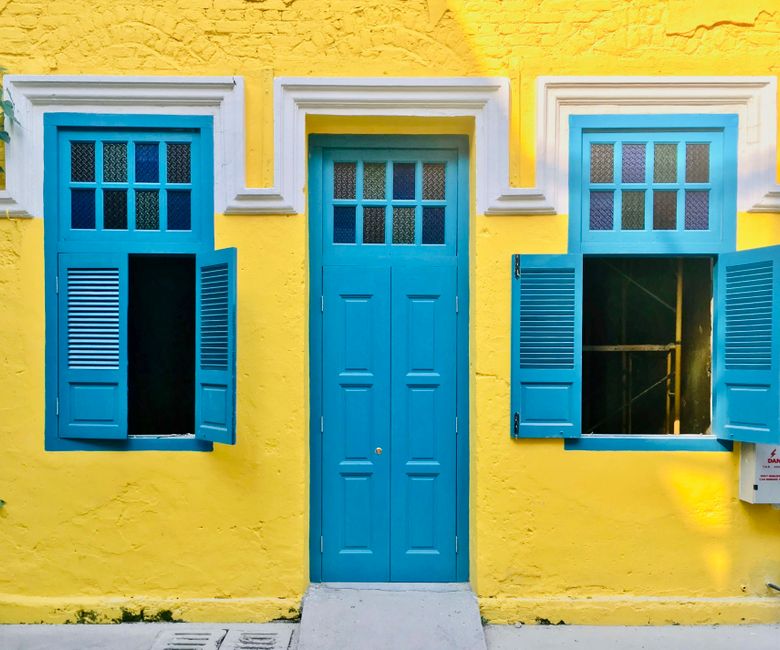 A yellow painted wall with a blue door and windows