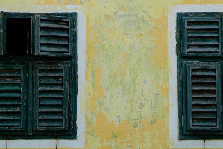 Wooden louvered shutters on a faded yellow wall